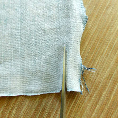 image of denim fabric and scissors cutting a strip