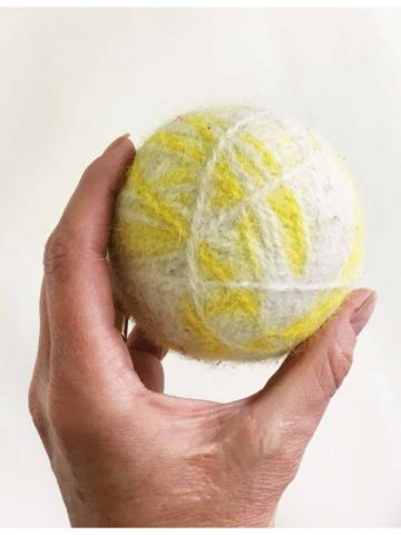 image of a hand holding a yellow and white wool dryer ball