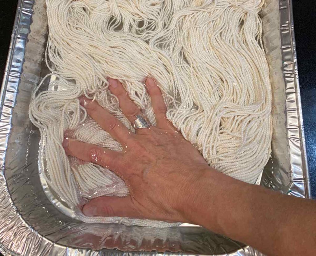 image of a hand pushing white yarn down in water